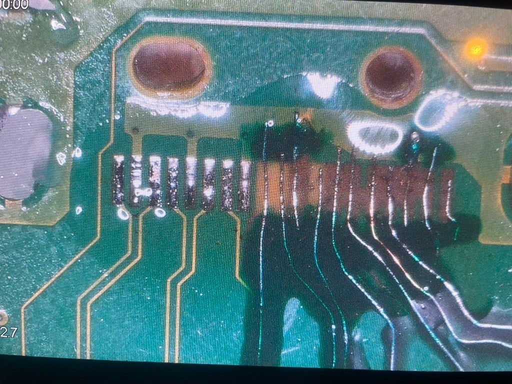 Microscope view of corroded solder pads on a console mainboard